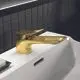Waschtischarmatur in Brushed Gold-Finish von Ideal Standard, gefertigt mit einem langen Auslauf und moderner Hebelform, montiert auf einer weißen Oberfläche neben einer Seifendose.